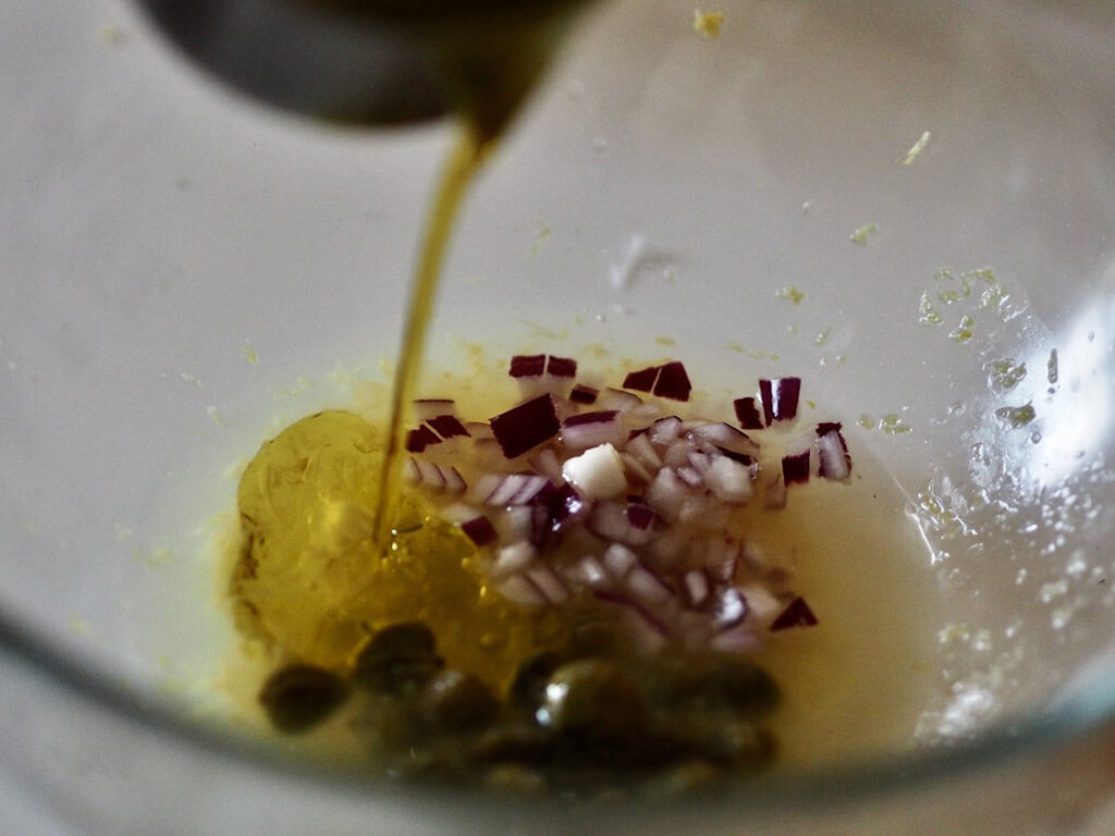 Lasikulhossa sekoittuneena pilkottu punasipuli, oliiviöljy, kaprikset, sitruunanmehu sekä -kuori.